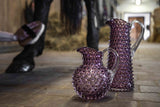 Underlay Violet Hobnail Jug Tall on a white stone floor with a stable and horse in the background